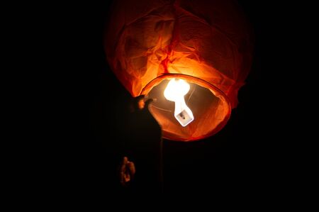 A red coloured sky lantern with the flames showing clearly lifiting offの写真素材