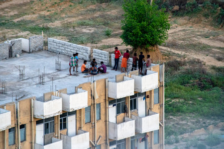 Delhi, India - circa 2020 : Men in relaxed wear standino on the rooftop of a low cost housing project watching the feilds. Shows the projects for lower economic households like maids, drivers, laborers, contractors and more in Gurgaonのeditorial素材