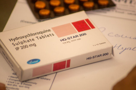 Photograph of a box and tablets of a hydroxychloroquine sulphate tablets on a piece of white prescription paper with a pen on the paper.のeditorial素材