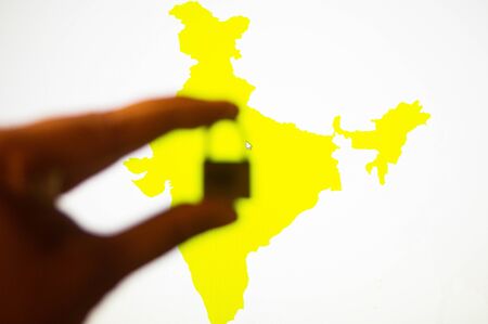 Photograph of the map of india on a white board in yellow colour with a hand holding a lock in front of itの写真素材