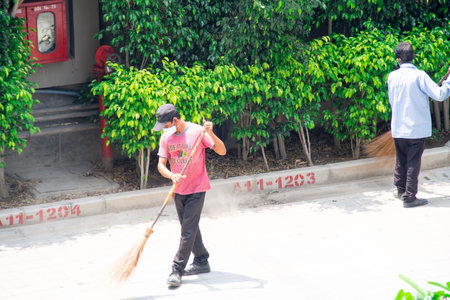 Male sweeper in blue uniform cleaning street and sidewalks with long broom in a society as part of swachh bharat cleanliness and sanitization for corona covid19のeditorial素材