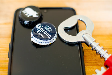 Mobile phone on a wooden board with beer bottle caps and an opener showing online app for alcohol...