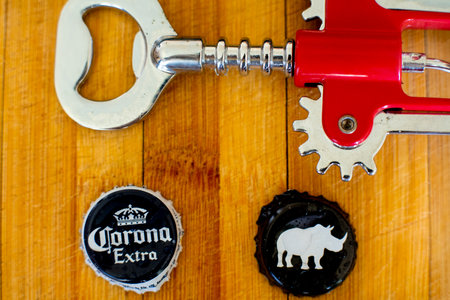 Shot of wooden board with mobile phone, bottle opener, and beer bottle caps of corona and white rhinoのeditorial素材