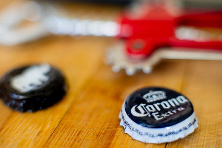 Shot of wooden board with mobile phone, bottle opener, and beer bottle caps of corona and white...