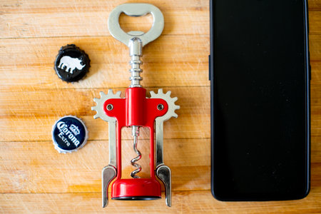 Shot of wooden board with mobile phone, bottle opener, and beer bottle caps of corona and white rhinoのeditorial素材