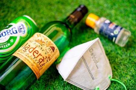 Gurgaon, Haryana, India - circa 2020 : Flatlay of alcohol liquor bottles on grass with a mask and...