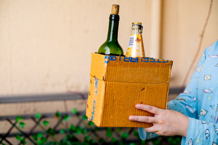 Gurgaon, Haryana, India - circa 2020 : Young indian girl carrying a cardboard box of alcohol liquor that has been home delivered through an online app. Shows concept of government guidelines to allow home delivery of alcohol liquor through online startupsのeditorial素材