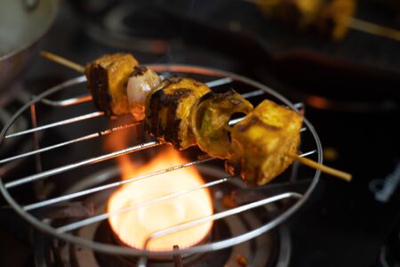 shot of paneer cottage cheese being burnt charred tandoori grilled over a meal grill and a gas stove with flames coming up and burning the cheese, peppers, onions and tomatoesの写真素材