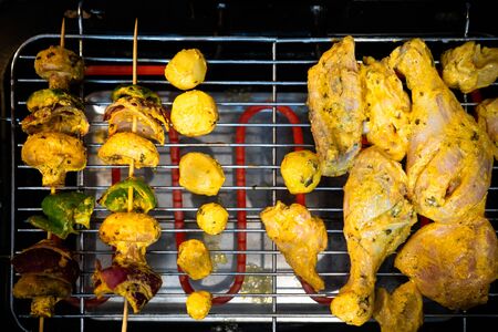 Top flatlay view showing chicken cooking on one side and vegetables cooking on the other over a electric grillの写真素材