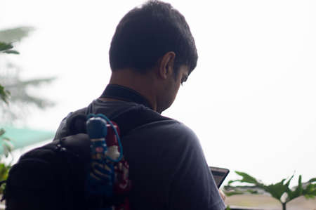 Young indian male with a backpack, umbrellas looking at a mobile phone with a foggy winter...