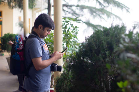 Young indian male in t-shirt messaging emailing connecting on mobile while on vacation with a...