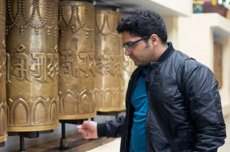 Young indian man turning a buddhist prayer wheel at a monastry temple in mcleodganj himachal india