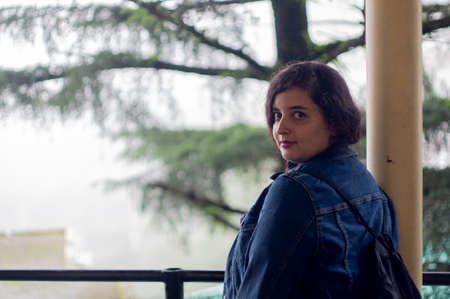 Young indian woman turning around and looking with beautiful fir trees fading in the fog behind her