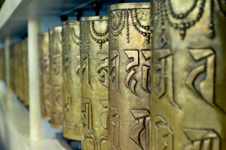 Religious copper buddhist prayer wheels with a prayer mantra written on it in a pilgamage spot in a monastaryの写真素材