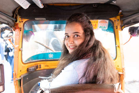 Young indian girl driving an autorickshaw smiling looking back