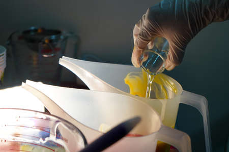 White latex gloved hand pouring a small beaker of liquid fragrance oil, water, chemical and more into a solution, food or baking mixの写真素材