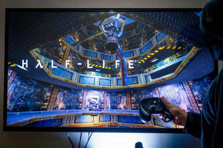 Man holding a steam controller and playing popular video game Half life on a television and PCのeditorial素材