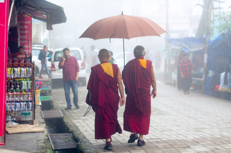 Bhuddist monks in red and yellow holding an umbrella in the foggy people filled streets of dharamshala himachal pradesh indiaのeditorial素材
