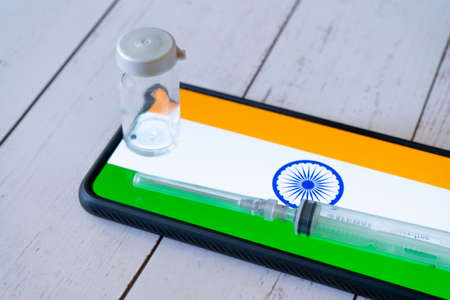 mobile phone with app showing indian flag with a syringe and small glass bottle vial of medicine...