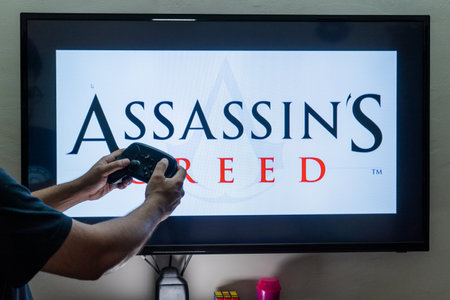 Man holding steam controller in front of a screen loading a game of assassins creed an action adventure game by ubisoft with multiple installementsのeditorial素材