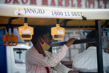 Man in public transport electric auto rickshaw sitting with mask pulled over chin during the...
