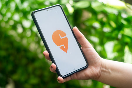 Mobile phone with swiggy held by woman, showing this food delivery food tech startup with cloud...