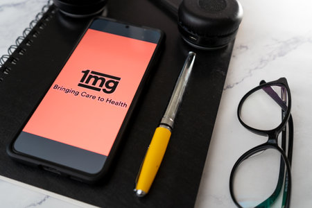Flatlay shot showing a mobile phone with the app of 1Mg a home medicine delivery online technology application with notebook, headphones, specs and pen showing financial research for this unicornのeditorial素材
