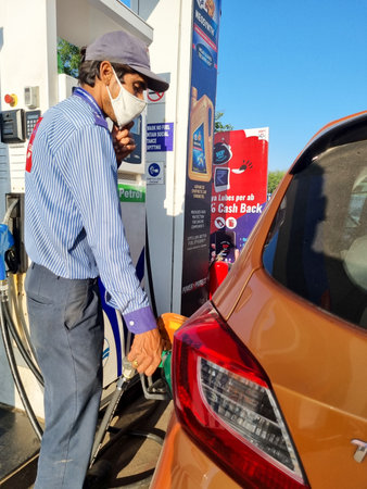 indian man at fuel station filling gas petrol diesel into an orange car highlighting the increasing prices of fuel in Indiaのeditorial素材