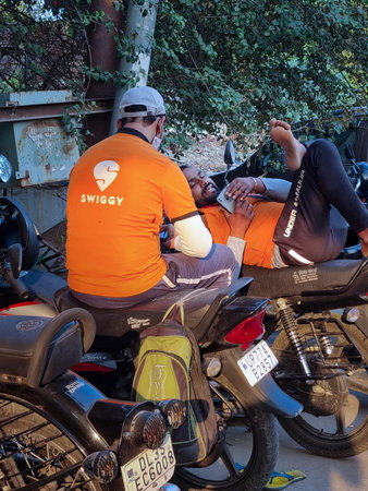 Swiggy food delivery rider sitting on bike waiting for order takeaway in orange shirt while people roam aroundのeditorial素材