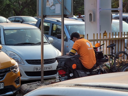Swiggy food delivery rider takes a break on bike while waiting for order preparation at restaurant showing scale of this food tech startupのeditorial素材
