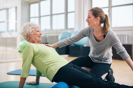 Physical therapist working with a senior woman at rehab. Female trainer helping senior woman doing exercise on foam roller at gym. Physical therapist working with a senior woman at rehab. Female trainer helping senior woman doing exercise on foam roller at gym.