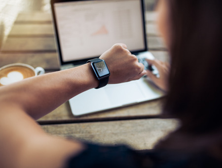 Close up shot of a woman checking time on her smartwatch. Female sitting in cafe with a laptop and cup of coffee. Close up shot of a woman checking time on her smartwatch. Female sitting in cafe with a laptop and cup of coffee.