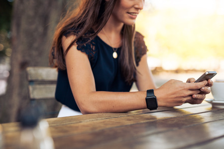 Woman typing text message on smart phone in a cafe. Cropped image of young woman sitting at a table with a coffee using mobile phone. Woman typing text message on smart phone in a cafe. Cropped image of young woman sitting at a table with a coffee using mobile phone.