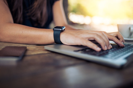 Hands of woman wearing smartwatch on the keyboard of her laptop computer. Female working on laptop in a cafe. Hands of woman wearing smartwatch on the keyboard of her laptop computer. Female working on laptop in a cafe.