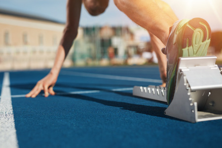 Feet on starting block ready for a spring start. Focus on leg of a athlete about to start a race in stadium with sun flare. Feet on starting block ready for a spring start. Focus on leg of a athlete about to start a race in stadium with sun flare.