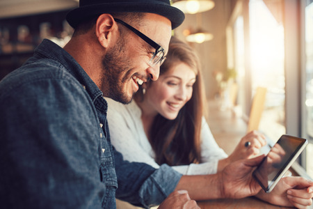 Close up portrait of happy young couple using a digital tablet together at a coffee shop. Young man and woman looking at touch screen computer and smiling. Close up portrait of happy young couple using a digital tablet together at a coffee shop. Young man and woman looking at touch screen computer and smiling.