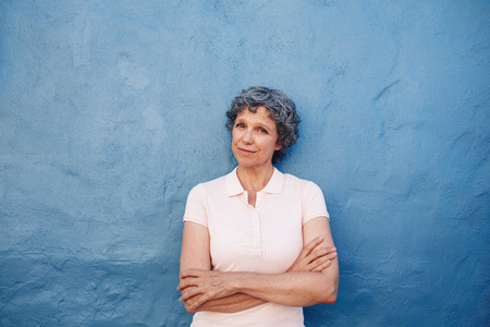 Portrait of beautiful senior woman standing with her arms crossed against blue wall. Happy mature female looking at camera. Portrait of beautiful senior woman standing with her arms crossed against blue wall. Happy mature female looking at camera.