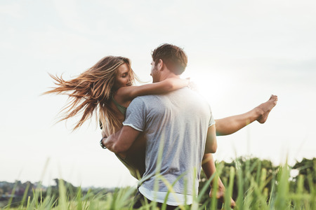 Shot of young man carrying his girlfriend in his arms on grass field. Couple having fun in nature on a summer day. Shot of young man carrying his girlfriend in his arms on grass field. Couple having fun in nature on a summer day.