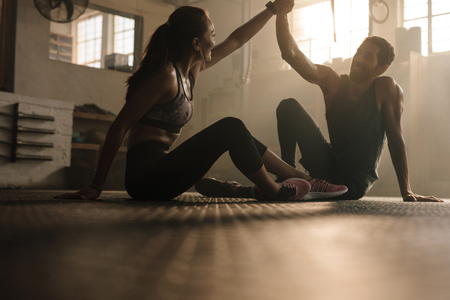 Fit man and woman sitting on floor and high fiving at the gym. Fitness couple after successful workout session in gym.