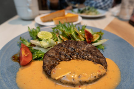 Beef steak with sauce and salad on a blue plate in a restaurantの写真素材