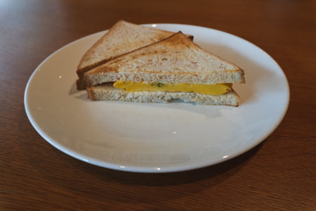 Sandwich with egg and cheese on white plate on wooden table.の写真素材