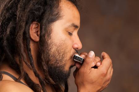 rastafarian man playing mouth harmonicaの写真素材