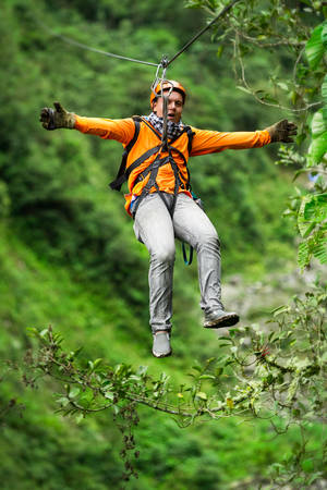 adult tourist on zipline dressed in orange against green backgroundの写真素材