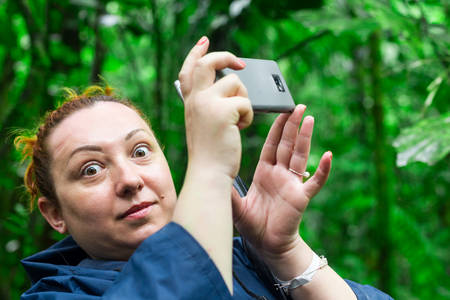 Funny face of tourist woman into the jungle while snapping a photo with her mobile phone