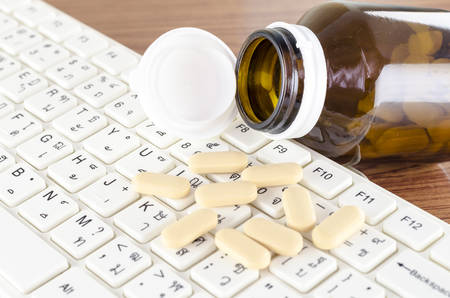 pills on keyboard computer on wooden background concept technology addiction