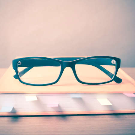 book with sticky note and eyeglasses on wood background vintage styleの写真素材