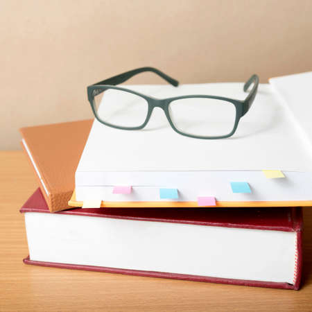 book with sticky note and eyeglasses on wood background