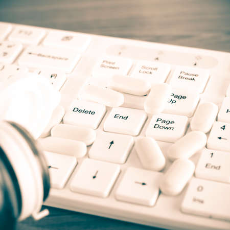 pills on keyboard computer on wooden background concept technology addiction vintage styleの写真素材