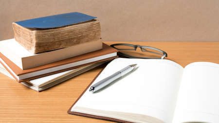 open notebook with stack of book on wood background