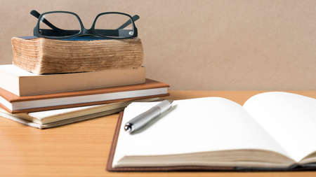 open notebook with stack of book on wood backgroundの写真素材